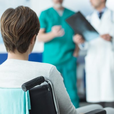 Professional doctors examining a disabled patient's x-ray and nurse pushing a woman on wheelchair, healthcare and disability concept